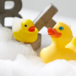 Zwei Badeenten küssen sich, leicht im Schaum dümpelnd, in einer Badewanne.