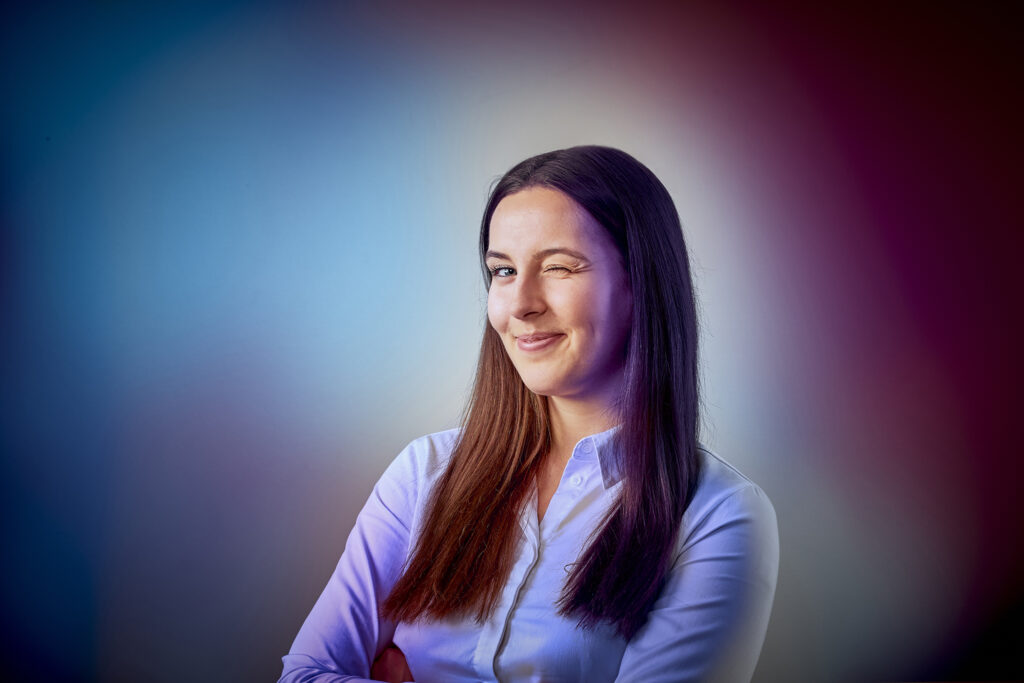 Eine junge Frau, guckt in die Kamera und zwinkert mit ihrem linken Auge den Betrachter an. Das Bild ist verfremdet mit den Farben, rot, magenta und blau.