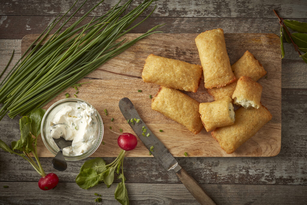 Kartoffeltaschen mit Frischkäsefüllung liegen auf einem kleinen Holzbrettchen mit einem Messer daneben.